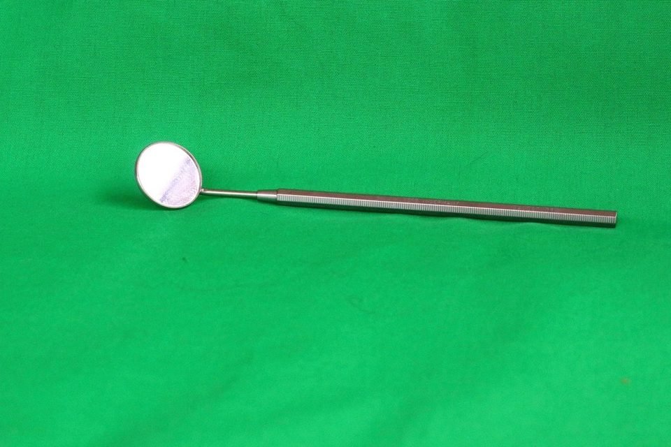 Dental mirror on a green background, the kind of tool a dentist uses to check a loose crown